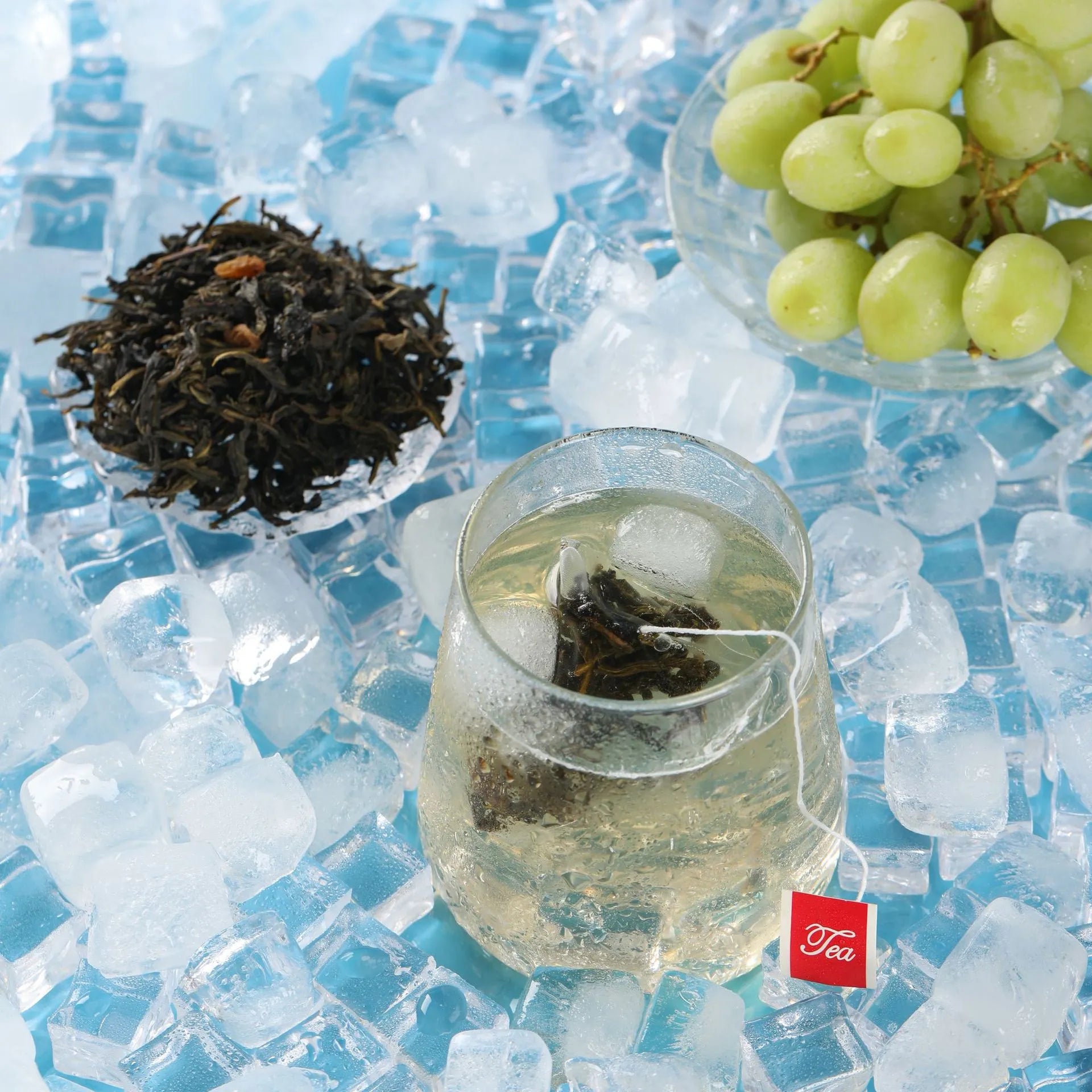 Top view of grape oolong cold brew tea with ice cubes, green grapes, and dry leaves