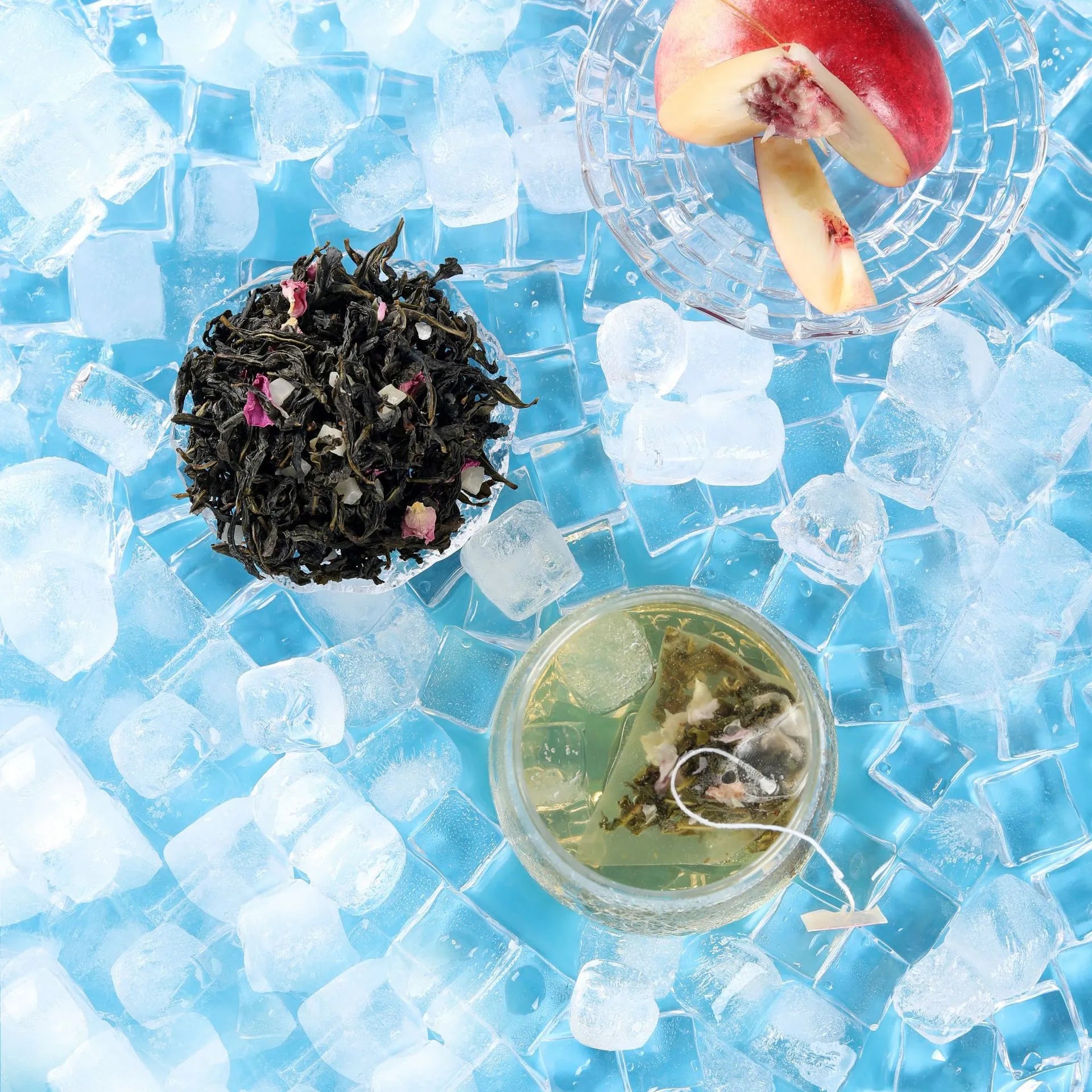 Top-down composition featuring cold brew white peach oolong tea bag in glass, loose tea leaves, fresh peach, and ice cubes