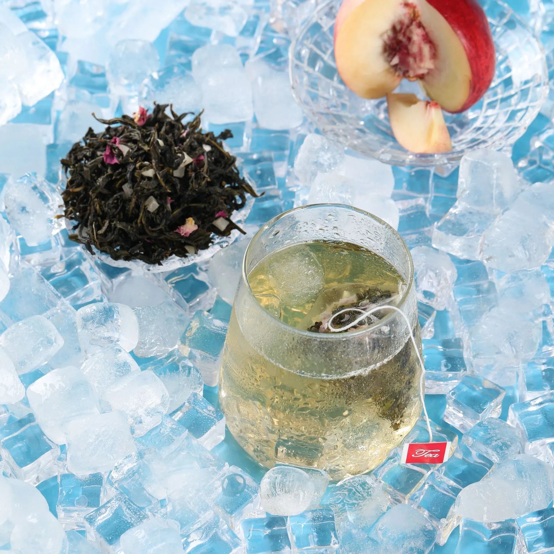 A cold brew tea bag of Leafmill White Peach Oolong soaking in a glass, surrounded by ice cubes and fresh peach slices