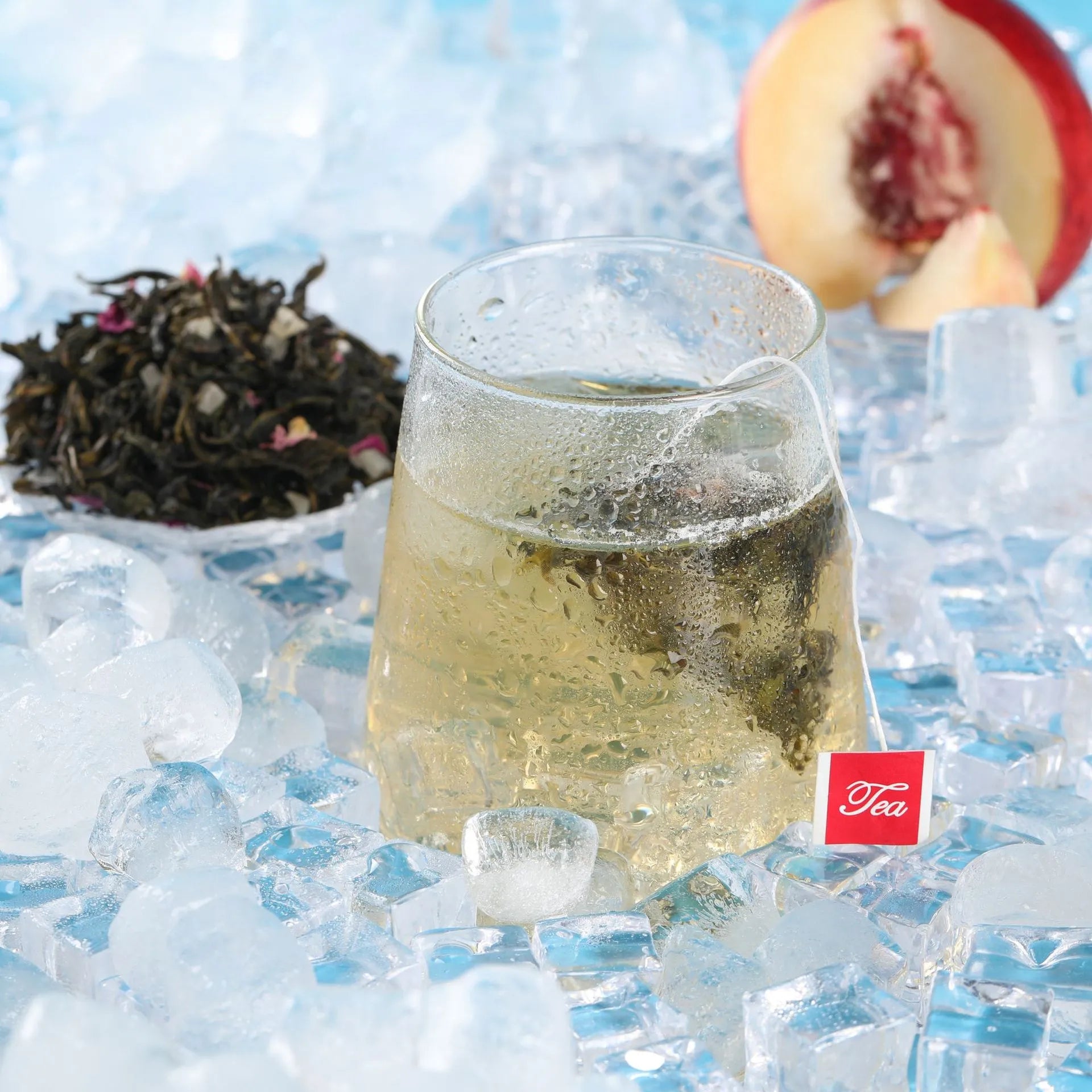 Close-up of condensation-covered glass with Leafmill White Peach Oolong tea bag, surrounded by ice cubes and loose tea leaves