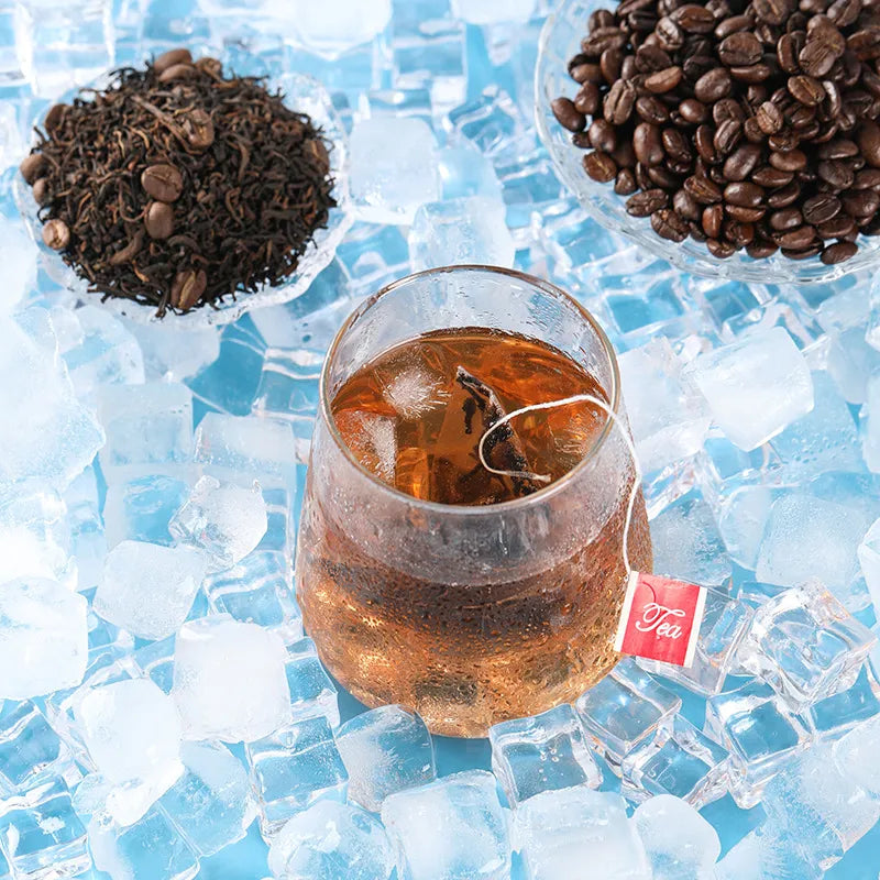 Close-up front view of a dewy cold brew tea glass with pu-erh tea and coffee beans in the blurred background.