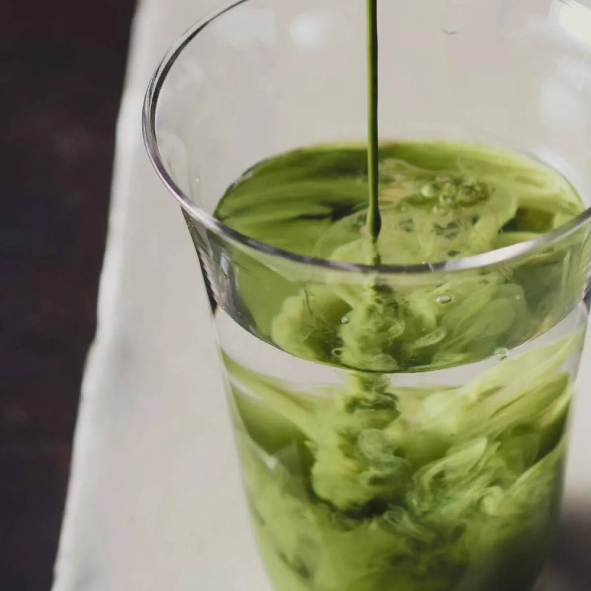 Vivid green Leafmill matcha being poured into a glass of water, symbolizing natural energy and wellness benefits.