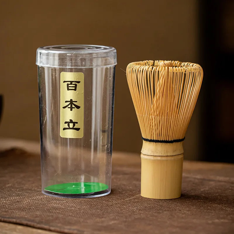 Bamboo chasen (matcha whisk) with a clear plastic storage case, featuring a gold label with Japanese characters "百本立" (Hyakubon Dachi, indicating the 100 - prong design) for traditional Japanese tea ceremony.