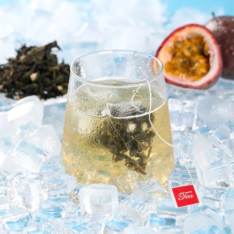 A close-up of a glass of cold brewed passion fruit oolong tea with a tea bag, surrounded by ice cubes and fresh passion fruit.